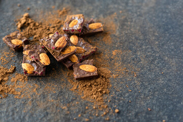 Broken pieces of almond chocolate and cocoa powder on a wooden background