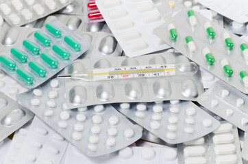 A pile of medical pills and capsules and a thermometer