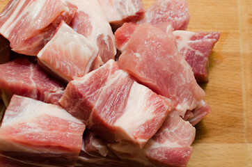 Raw pork, lying on a wooden board, cut into small cubes and ready to marinate. Close-up
