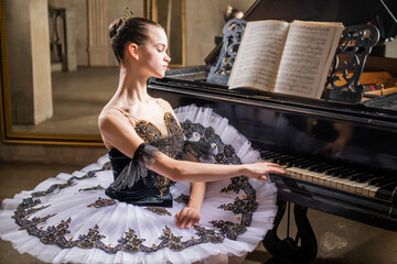 Young ballerina in white tutu plays a beautiful old piano