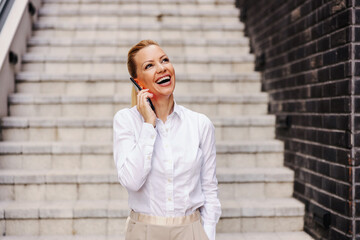 Smiling cheerful attractive blond fashionable woman standing outdoors and talking on the phone.