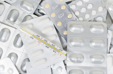A pile of medical pills and capsules and a thermometer