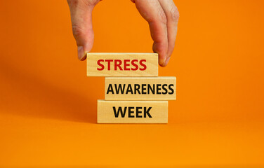 Stress awareness week symbol. Wooden blocks with words 'Stress awareness week'. Beautiful orange background. Doctor hand. Psychological, business and stress awareness week concept. Copy space.