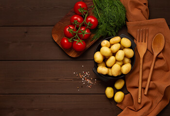 Young potatoes, raw, in a cast iron skillet, on a wooden background, top view, horizontal,