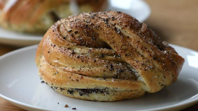 Freshly baked cardamom bun being placed on a white plate. In the background is cinnamon bun. Footage made in Sweden.