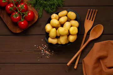 Young potatoes, raw, in a cast iron skillet, on a wooden background, top view, horizontal,