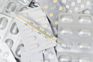 A pile of medical pills and capsules and a thermometer