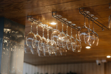 Clean glasses for alcoholic beverages hang over the bar in a modern restaurant.