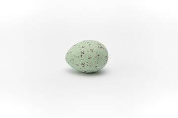 One light green chocolate egg imitating quail egg with specks on a white background. Minimalistic decoration for Easter. Sweets for the holiday