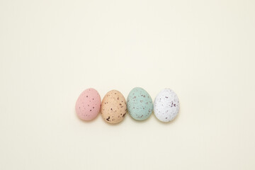 Four chocolate eggs, white, red, green and yellow with crumples on a light yellow background. Imitation of quail eggs. Painted eggs for Easter