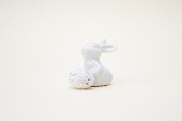 Porcelain rabbit with a chocolate egg imitating a quail egg on a white background. Easter decoration