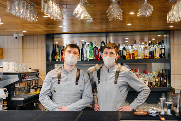 Two stylish bartenders in masks and uniforms during the pandemic, stand behind the bar. The work of restaurants and cafes during the pandemic.