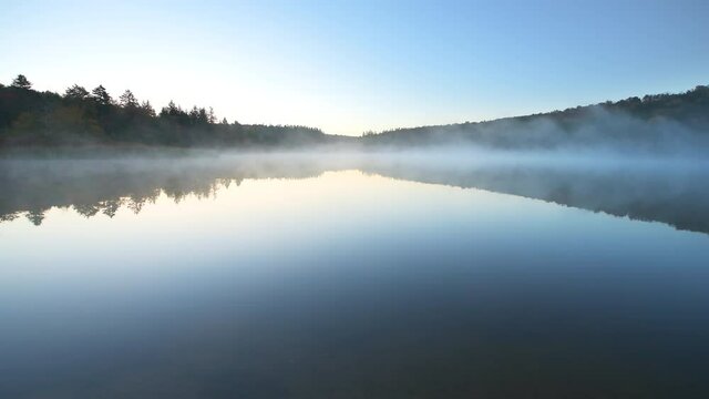 Wide angle panning view of Spruce Knob Lake in Appalachian mountains of Canaan valley in West Virginia with sunrise morning mist fog floating above water in Monongahela National Forest in autumn fall