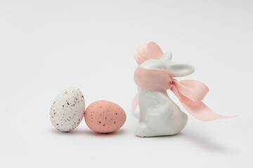 Two chocolate eggs, white and red with specks on a white background. Imitation of quail eggs. Porcelain rabbit with a pink ribbon covering the muzzle