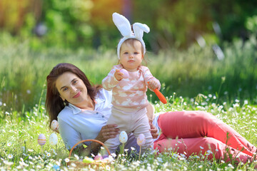 Happy family celebrate Easter, enjoying picnic in spring garden. Parent, baby Kid have fun after egg hunt outdoors in meadow. Woman play with toddler girl wearing bunny ears, gnaw carrot. copy space