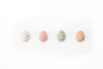 Four chocolate eggs, white, red, green and yellow with crumples on a white background. Imitation of quail eggs. Painted eggs for Easter