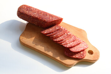 Slices of salami pepperoni on wooden cut board on white background. Top view, copy space