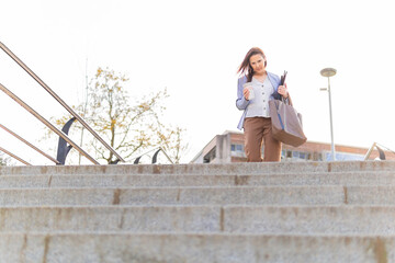 Young adult beautiful businesswoman drinking coffee in the street leaving work with coffee to go...