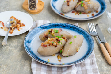 Traditional Lithuanian dish Zeppelin, boiled potato dumplings stuffed with minced pork, on a colored ceramic plate on a gray concrete background.