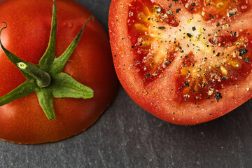 cut tomato with pepper and salt on a black slate background
