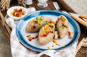 Traditional Lithuanian dish Zeppelin, boiled potato dumplings stuffed with minced pork, on a colored ceramic plate on a gray concrete background. © Natallya_ph