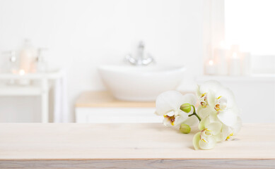 Fototapeta na wymiar Orchid flowers on wooden table in blurred spa salon bathroom