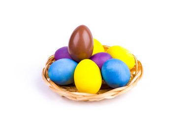 Easter chicken eggs painted in different colors and one chocolate in a wicker basket on a white background.