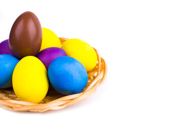 Easter chicken eggs painted in different colors and one chocolate in a wicker basket on a white background.