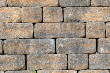 A stone wall made of old yellow bricks. No mortar was used between the bricks. Sunny day, closeup view.