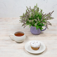 Fototapeta na wymiar Cupcake and coffee tea mug on a background of mint flowers on a white wooden table. Tea party with a cupcake.