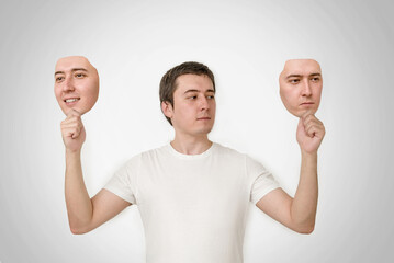 bipolar personality disorder. split personality, two-faced person. a man holds two face masks in his hands.