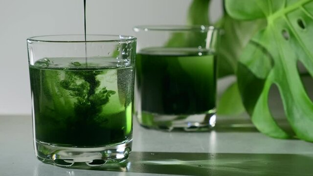 Chlorophyll extract is poured in pure water in glass against a white grey background with green leaf. Liquid chlorophyll in a glass of water. Concept of superfood, healthy eating, detox and diet