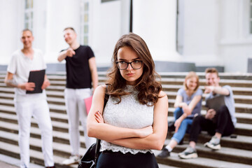 Angry and upset college girl standing with her hands crossed, being bullied by her group mates....
