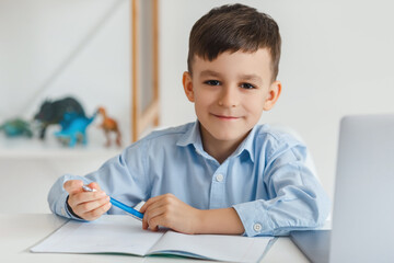 Clever kid doing homework using laptop and internet. Elementary school e-learning via video call....