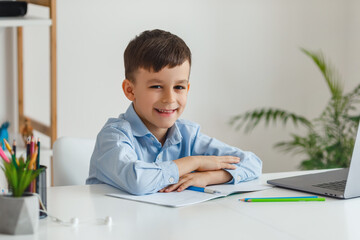 Clever kid doing homework using laptop and internet. Elementary school e-learning via video call. Boy studying online at home