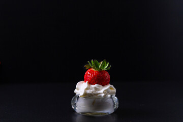 A strawberry partially dipped in a bowl containing whipped cream. All with a black background.