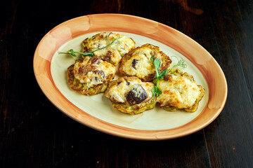 A traditional Ukrainian dish is zucchini pancakes with baked cheese and mushrooms, served in a plate on a dark wooden background.