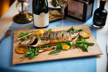 Roasted gourmet fish on the wooden board with wine on the restaurant table