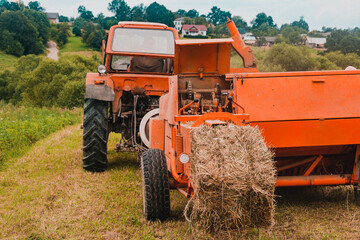 Old tractor in the field, forage harvesting for the winter, press and hay, pressing dry grass.