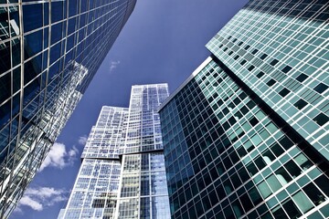 Office and residential skyscrapers against bright sun and clear blue sky close up. Reflections and glare on the glass facades of modern skyscrapers close-up. Modern buildings exterior design. 