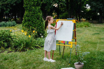 A schoolgirl writes lessons on a blackboard and is engaged in outdoor training. Back to school, learning during the pandemic