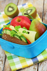 Healthy lunch box with whole grain roll with Swiss cheese, lettuce, tomato and cucumber; apple and kiwi fruit
