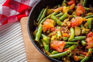 stewed green beans in a cast iron skillet on a white wooden rustic background
