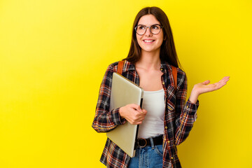 Young caucasian student woman holding a laptop isolated on pink background showing a copy space on...