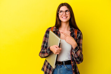 Young caucasian student woman holding a laptop isolated on pink background smiling and pointing...