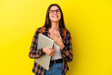 Young caucasian student woman holding a laptop isolated on pink background laughs out loudly keeping hand on chest.