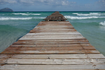 Long wooden pier entering into the wavy sea on a sunny day in Alcudia, Mallorca