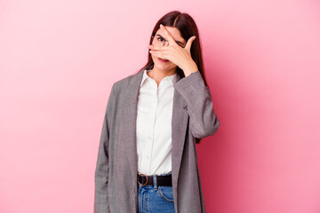 Young caucasian business woman isolated on pink background blink at the camera through fingers, embarrassed covering face.