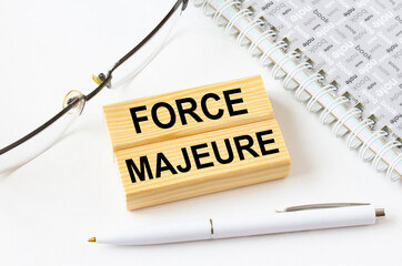Text Force Majeure on a wooden blocks lying near notepad with eyeglasses and pen
