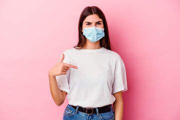 Young caucasian woman wearing a mask for virus isolated on pink background person pointing by hand to a shirt copy space, proud and confident